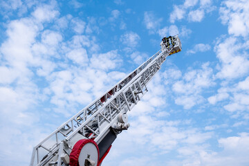 Une grande échelle de pompier pour sauver des vies sur fond de ciel bleu avec des nuages - obrazy, fototapety, plakaty