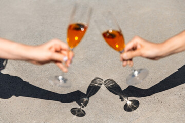 celebration, party and shadows concept - close up of hands clinking wine glasses on sunny day