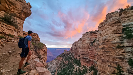 Rear view of man with backpack hiking along Bright Angel trail with panoramic aerial overlook of South Rim of Grand Canyon National Park, Arizona, USA, America. Amazing vista after sunrise in summer