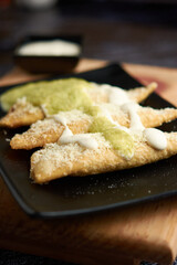 Empanadas with cheese, cream and green chili, placed on a plate, the green sauce and cream placed around it.