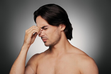Naklejka premium Portrait of frustrated young shirtless man massaging nose against grey background