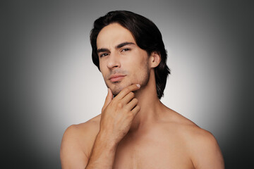 Portrait of young shirtless man holding hand on chin against grey background