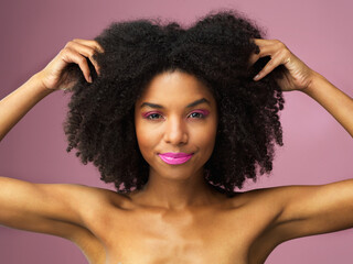 Face, hair care and black woman with afro in studio isolated on a pink background with eyeshadow. Hairstyle portrait, lipstick makeup and African female model with salon treatment for cosmetics.