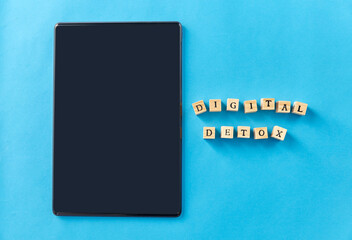 digital detox and technology concept - tablet pc computer and wooden toy block or stamps on blue background