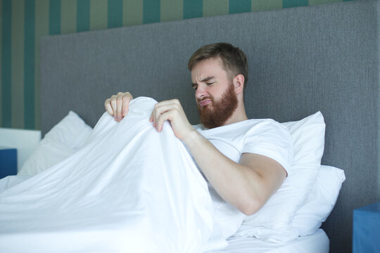 Young man worrying about his penis and erection failure, surprised guy is having trouble with his potency in bed in bedroom 