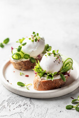 Poached egg sandwiches with cucumber and microgreens. Healty breakfast bruschetta on light background. Keto diet, text space