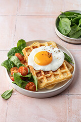 Savory breakfast with belgian waffles, fried egg and spinach, cherry tomato salad on pink tile background