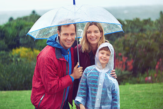 Happy, rain and portrait of a family with umbrella outdoor in nature for fun, happiness and quality time. Man, woman and boy child together with water drops and freedom while playing on vacation