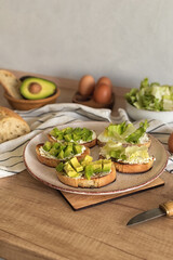 Ciabatta slices with cottage cheese and avocado pieces on a ceramic plate. Step 6 of the process of making healthy toast with avocado, cream cheese, boiled egg and green salad. Healthy lifestyle.