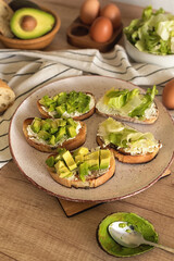 Ciabatta slices with cottage cheese and avocado pieces on a ceramic plate. Step 6 of the process of making healthy toast with avocado, cream cheese, boiled egg and green salad. Healthy lifestyle.