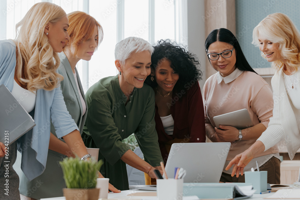 Sticker Group of happy mature women using laptop while discussing business in office together