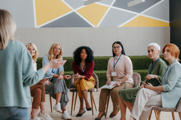 Group of confident mature women listening to speaker while visiting business conference - 602423501