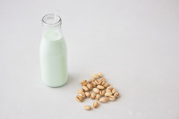 Pistachio milk in a bottle on a gray table next to pistachios. Vegetable milk. Nut milk for vegans