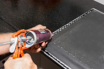 The plumber installs the sink. Applying sealant to the rim of a kitchen sink for countertop...