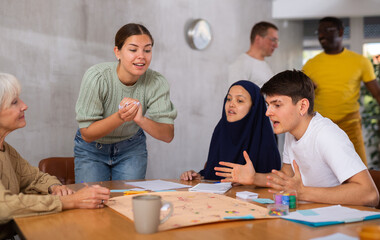 Happy young girl having fun with multiethnic group of friends, playing board game at table ..