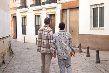 Real marriage of gay couple, holding hands in the street, with a gay pride flag in their pocket and seen from the back. Concept lgtb, lgtbiq+, couples, in love, pride.