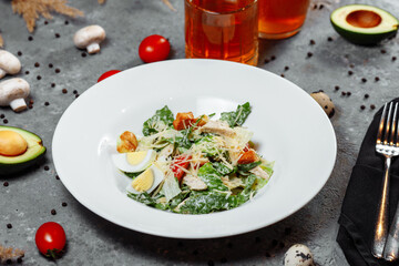 Traditional caesar salad in a white bowl on a old white table with leaves and a sauce boat and parmesan. Selected focus.