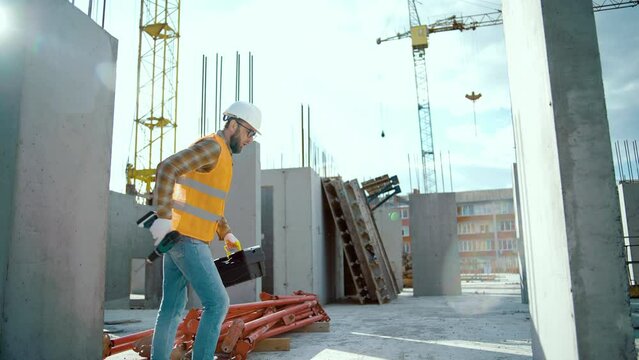 Happy construction worker at construction site dancing with boxtool and screwdriver. Enjoy the moment he wearing uniform and safety helmet. Looking at camera
