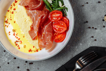 Crepes with fried egg, Jamon slices, fresh tomatoes and cucumber fillings on a white plate on an old wooden table, view from above