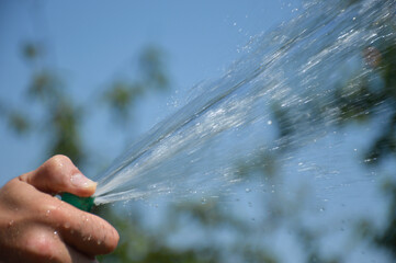 Man holding hose for watering plants in a garden. A powerful jet, a stream of clean water, drops...