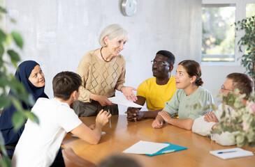 Fototapeta premium Group of multinational men and women discussing document while sitting at table in office..