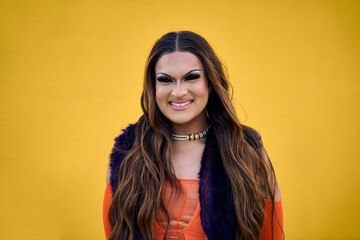 Portrait of smiling transgender young with yellow background. Happy Drag Queen person posing for photo on gay pride day. LGBT and trans community. Cheerful Caucasian people isolated and copy space. - obrazy, fototapety, plakaty