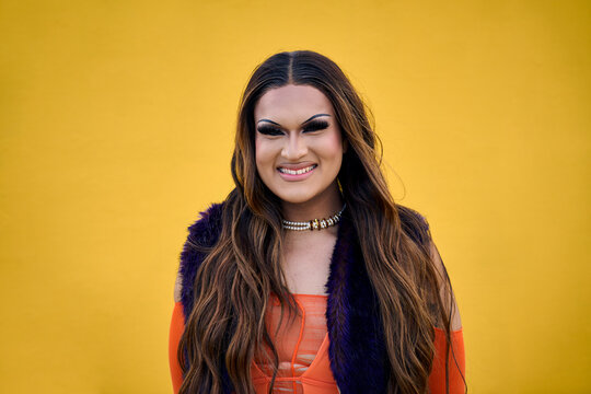 Portrait of smiling transgender young with yellow background. Happy Drag Queen person posing for photo on gay pride day. LGBT and trans community. Cheerful Caucasian people isolated and copy space.