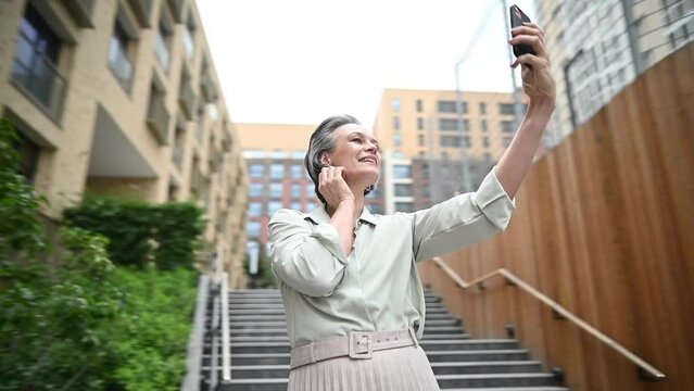 Mature caucasian woman takes a selfie on a smartphone in the street. The video rotates 360 degrees.