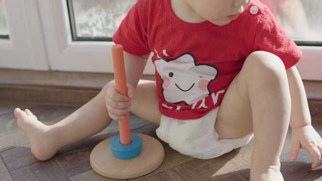 little toddler child red shirt playing wooden pyramid sitting floor near window indoor living-room daytime games. educational activities baby boy kid. white star on baby clothes. blue ring on stick
