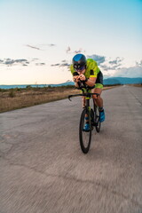 Obraz premium Triathlete riding his bicycle during sunset, preparing for a marathon. The warm colors of the sky provide a beautiful backdrop for his determined and focused effort.