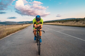 Triathlete riding his bicycle during sunset, preparing for a marathon. The warm colors of the sky...