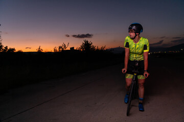 A triathlete rides his bike in the darkness of night, pushing himself to prepare for a marathon. The contrast between the darkness and the light of his bike creates a sense of drama and highlights the