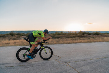  Triathlete riding his bicycle during sunset, preparing for a marathon. The warm colors of the sky provide a beautiful backdrop for his determined and focused effort.