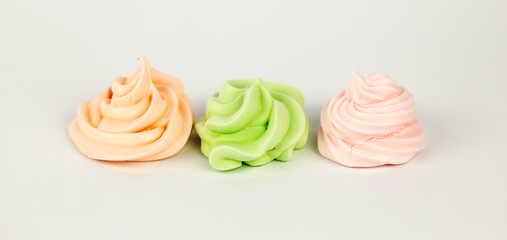 Obraz na płótnie Canvas Sweet pastry concept. Three meringues pink green orange on a white background. View from the front.