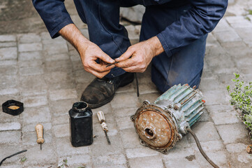 Elderly male professional worker, electrician, electromechanic repairs an old rusty electric motor...