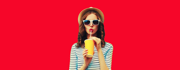 Portrait of stylish young woman drinking fresh juice wearing summer straw hat, sunglasses on red background - obrazy, fototapety, plakaty