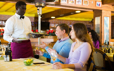 Dissatisfied guests conflicting with bewildered african american waiter because of poor quality of dishes in restaurant..