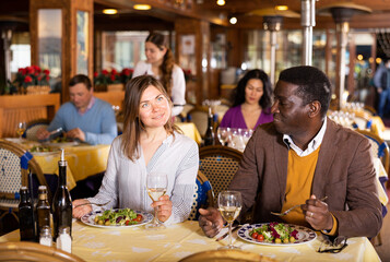 Positive couple, Caucasian woman and African-american man eating in restaurant and talking.