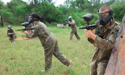 Fototapeta premium Excited male and female paintball players in protective uniform aiming and shooting with guns