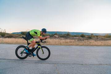 Fototapeta premium Triathlete riding his bicycle during sunset, preparing for a marathon. The warm colors of the sky provide a beautiful backdrop for his determined and focused effort.