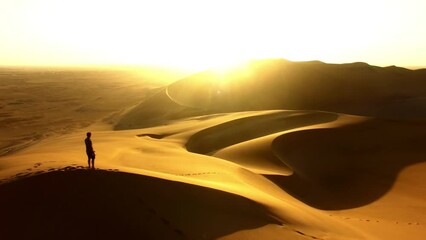 Travel, desert and silhouette of man at sunset with drone for destination, freedom or summer trip. Footprints, adventure and journey with guy on horizon of sand dunes on trip or Namibia vacation