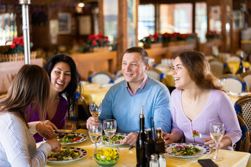 Group of people sitting at dining table in restaurant, chatting and laughing.