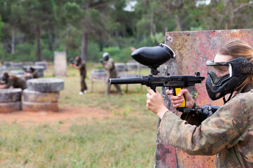 Fototapeta premium Paintball players of one team in camouflages and masks aiming with gun in shootout playing field