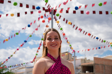 Blonde girl smiling. Happy young Caucasian woman dressed in a pink top, smiling joyfully, showing her happiness and well-being to someone. Body language. Young girl smiling at a festival. Party.
