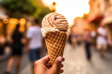 Foto auf Alu-Dibond female hand of adult woman holding ice cream cone in hand, in city on summer day with more people in background © wetzkaz