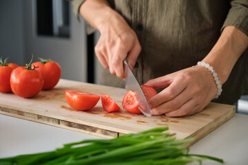 Unrecognizable young man cutting tomatoes at kitchen.