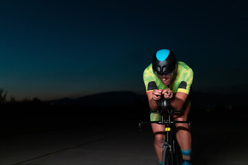 A triathlete rides his bike in the darkness of night, pushing himself to prepare for a marathon. The contrast between the darkness and the light of his bike creates a sense of drama and highlights the