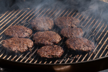 Grilling burgers on barbecue BBQ grill on hot charcoal. Homemade burger patties are being roasted on grill bars.