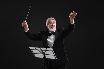 Professional conductor with baton and note stand on black background