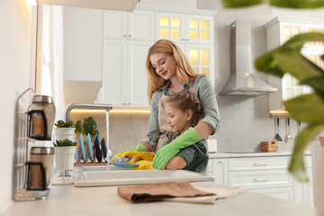 Mother and daughter in protective gloves washing plate above sink in kitchen